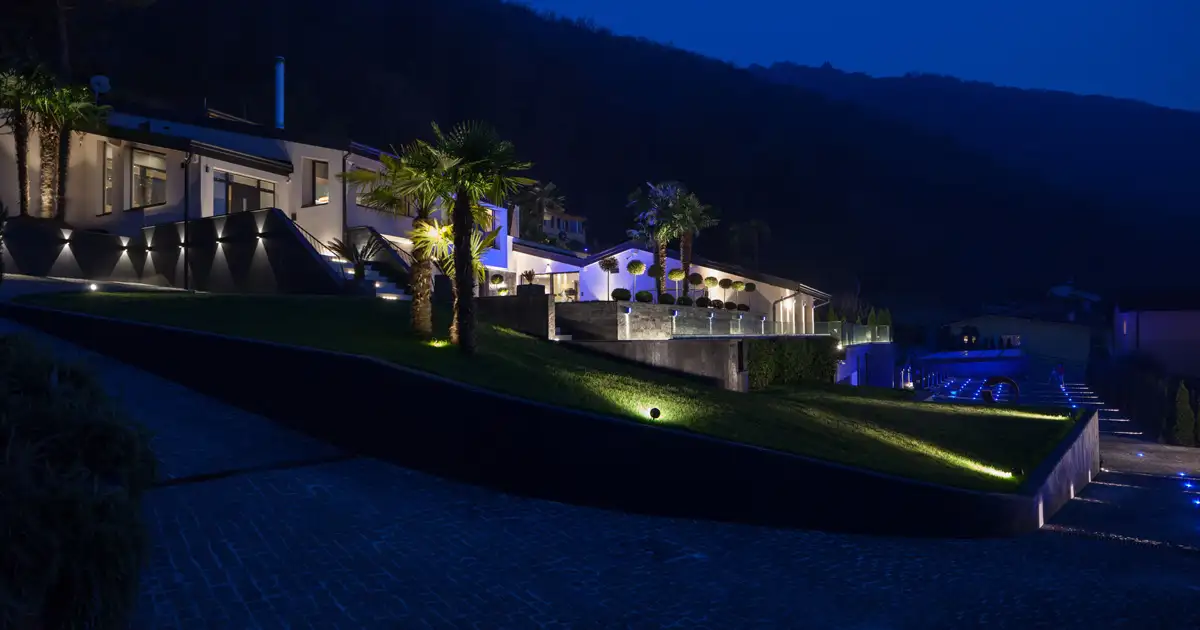 Luxury hillside home with architectural and landscape lighting highlighting outdoor spaces at night