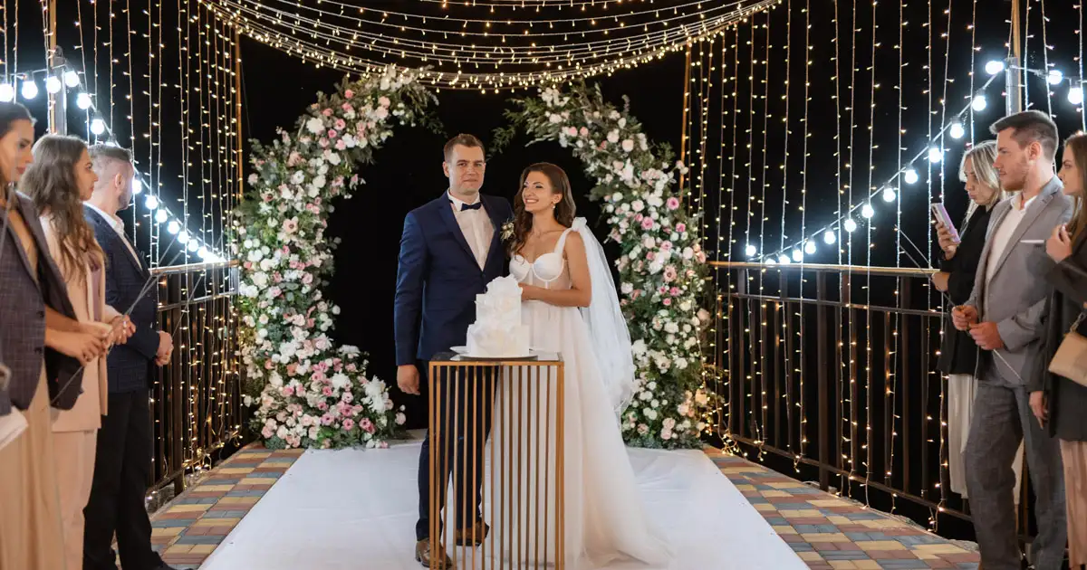 Outdoor wedding reception with hanging lights and guests enjoying illuminated celebration