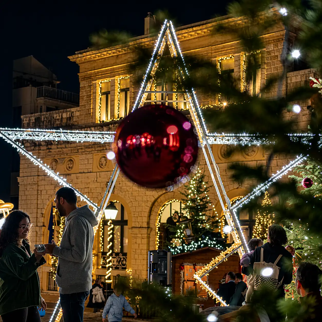 Outdoor holiday event with illuminated geometric decor and large ornament centerpiece in front of a lit historic building